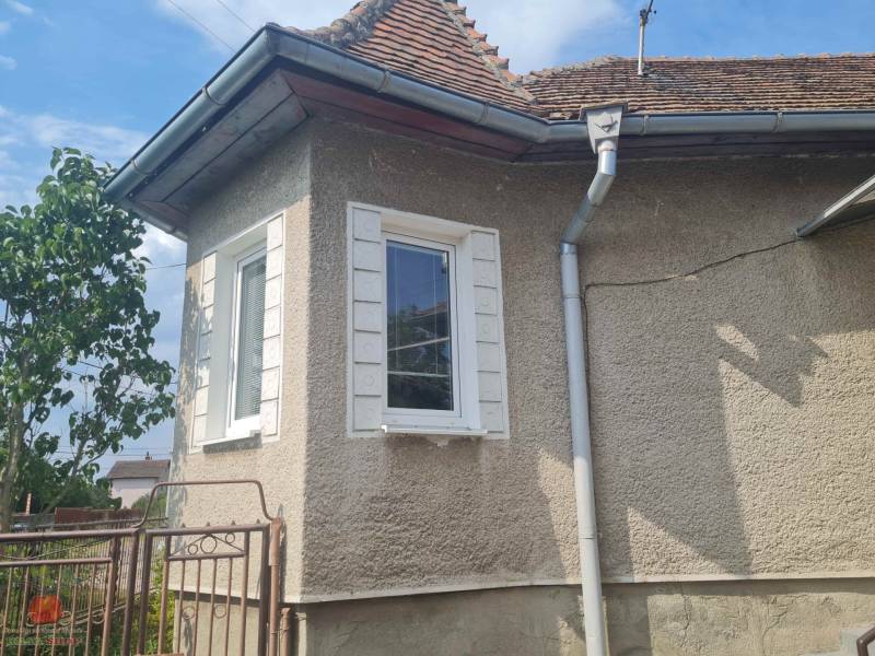 Rodinný dom v Komjaticiach, so šikmou strechou a bielym oknom, obklopený vegetáciou.