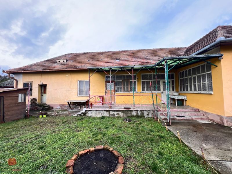 Žltý rodinný dom v Komjaticiach s priestrannou záhradou a kamenným chodníkom.
