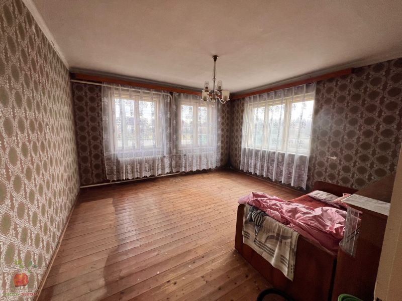 Izba v rodinnom dome s tapetami a podlahou s dreveným dekorom, cez okná závesy.