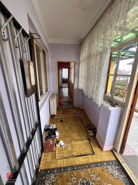 Chodba rodinného domu s topánkami, podlaha s dreveným dekorom, záclony a koberček.